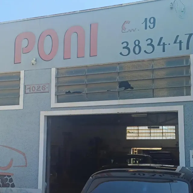 Fachada da oficina: PONI em vermelho, o telefone pintado, a placa 1026 em vermelho e o portão aberto com carros dentro