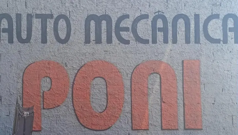 Letreiro pintado à mão na parede da oficina: AUTO MECÂNICA em grafite e PONI em vermelho, com o telefone pintado embaixo