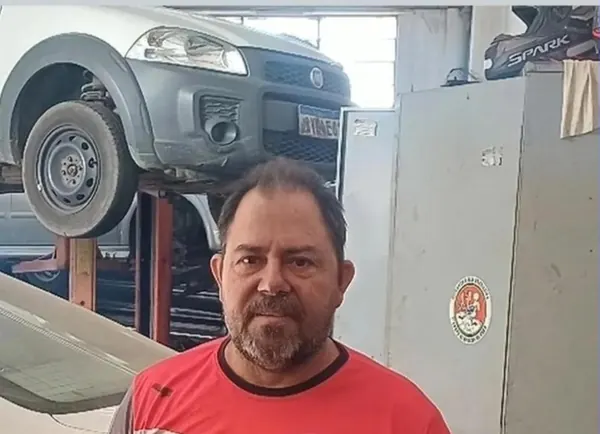 Mecânico de uniforme vermelho e preto da Auto Poni, com um carro no elevador ao fundo