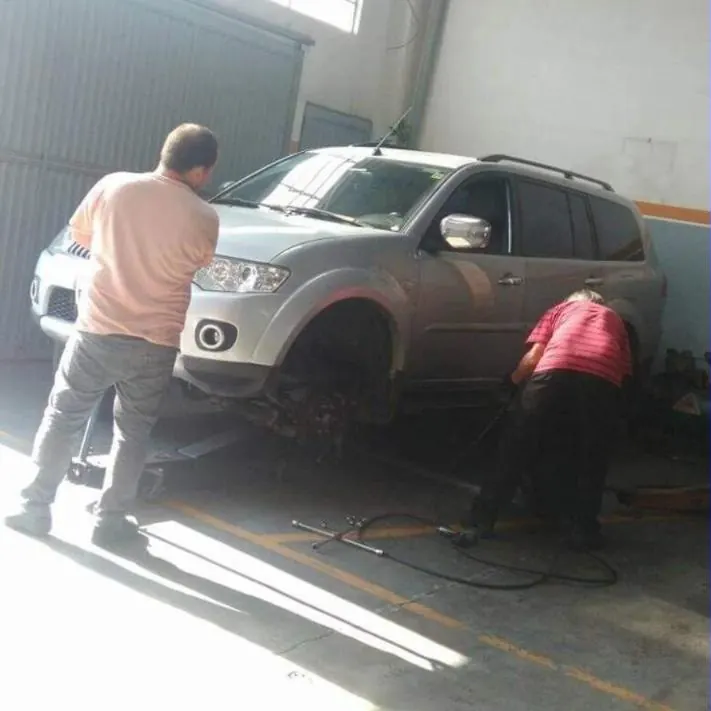 Dois mecânicos de costas trabalhando na roda dianteira de um utilitário prata
